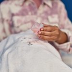 Femme versant du détergent liquide sur un vêtement avant lavage pour traiter une tache