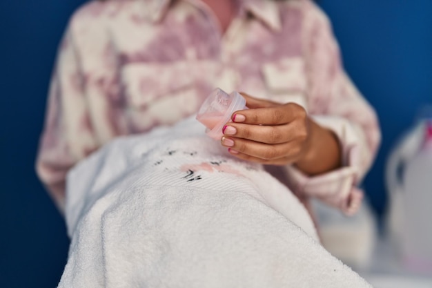 Femme versant du détergent liquide sur un vêtement avant lavage pour traiter une tache